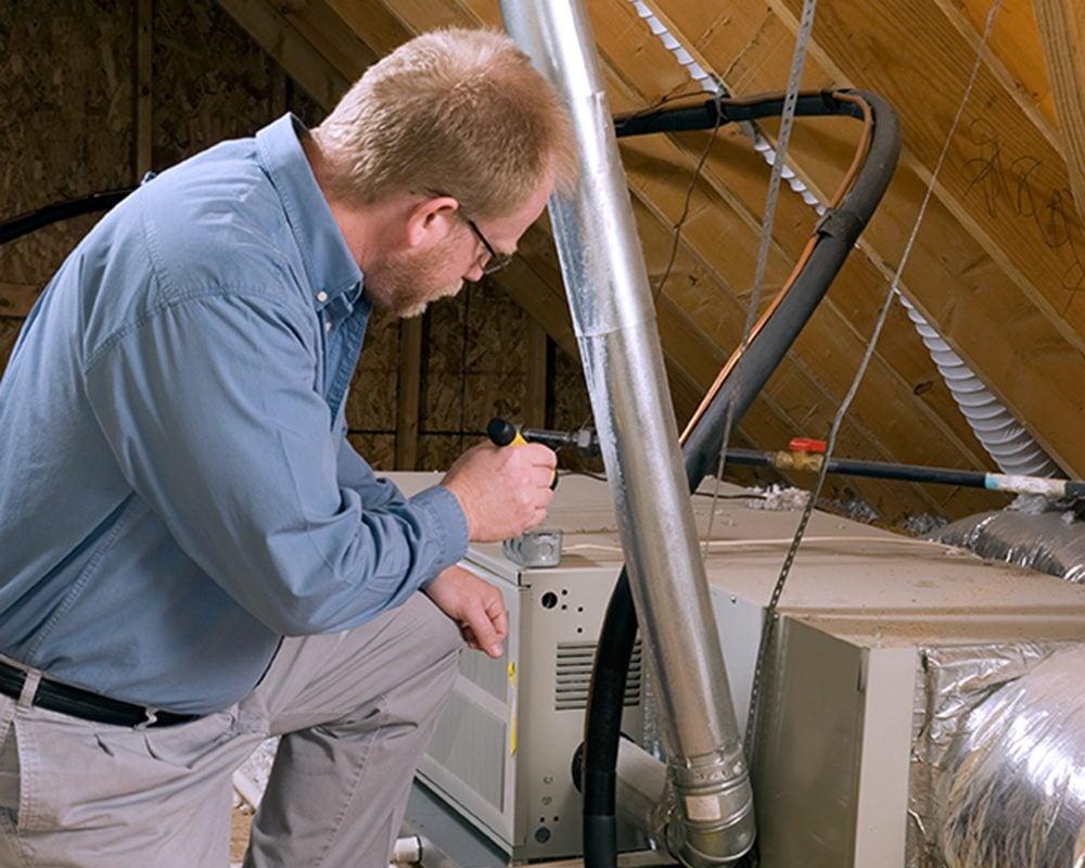 Technician servicing a downflow furnace installed in an attic